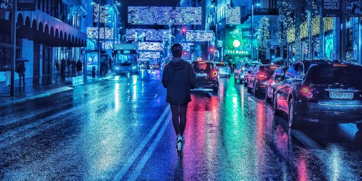 Person mit Helm läuft bei Nacht durch nasse, mit Neon beleuchtete Straße