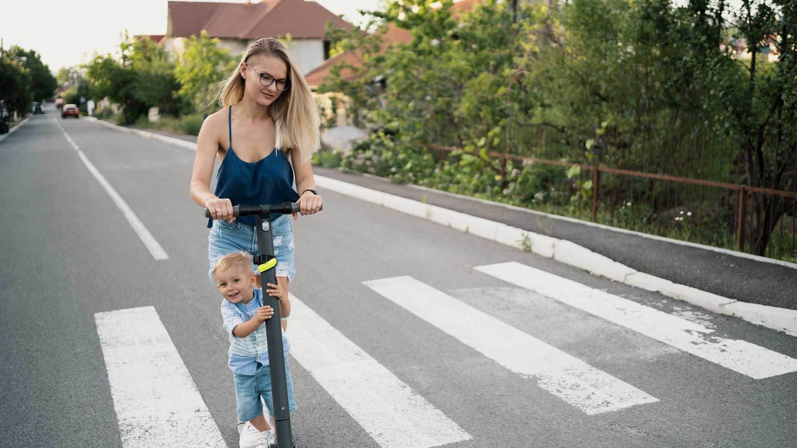 Junge Mutter fährt mit ihrem Sohn auf einem E-Scooter über einen Zebrastreifen