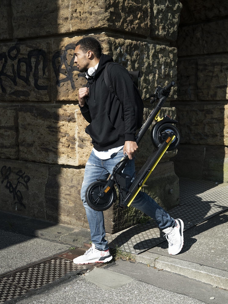 Mann trägt zusammengeklappten URBAN E-Scooter